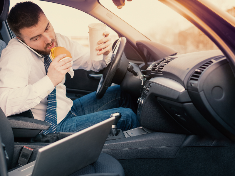 man eating, talking on the phone and looking at a device while driving